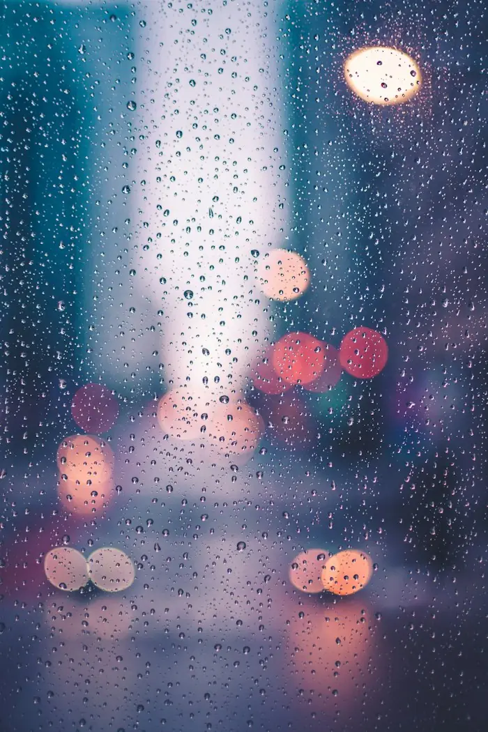 Rain on a window at night, with blurred city lights behind it